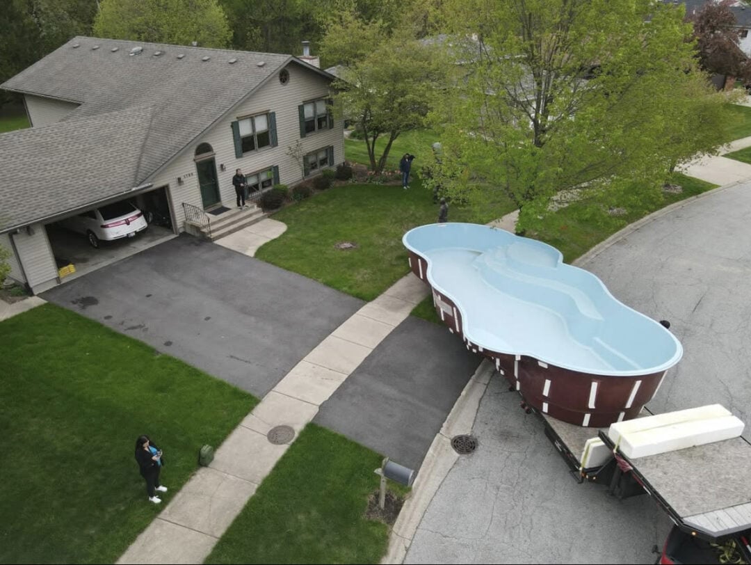 A freeform fiberglass pool being brought into a backyard.